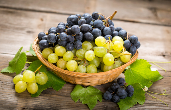 Photo of purple and green grapes in a woven basket sitting on a table. 