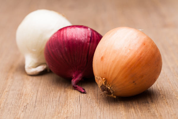 Photo of white, red and yellow onion on a table. 