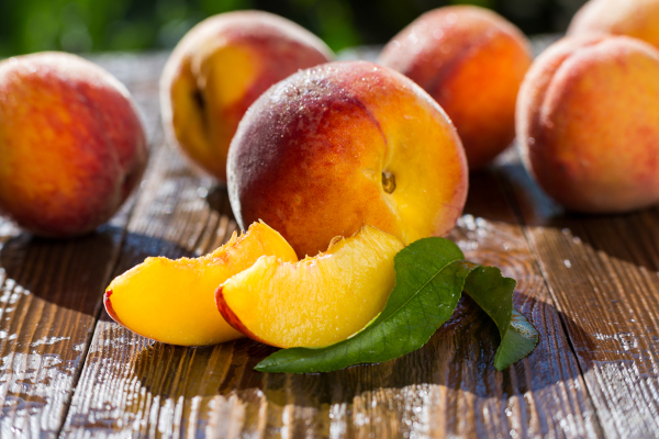 Photo of whole and sliced peaches on a table.