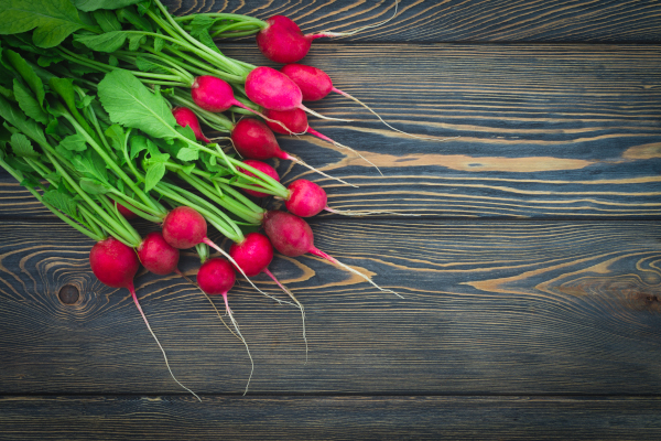 Photo of a pile of radishes with stem and leaves on a table. 